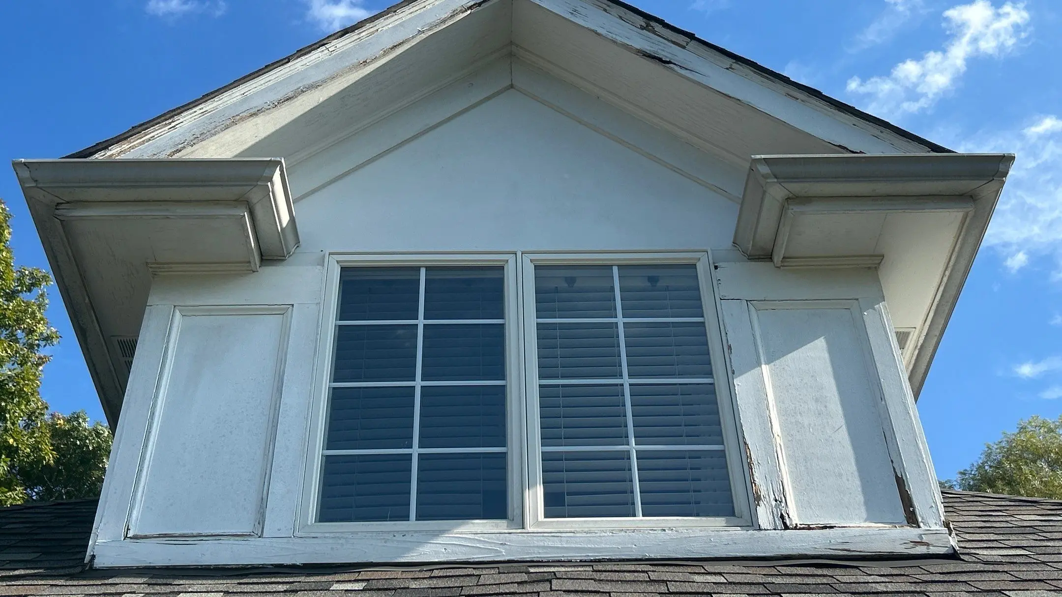 Peeling paint and deteriorated trim on dormer above asphalt shingle roof