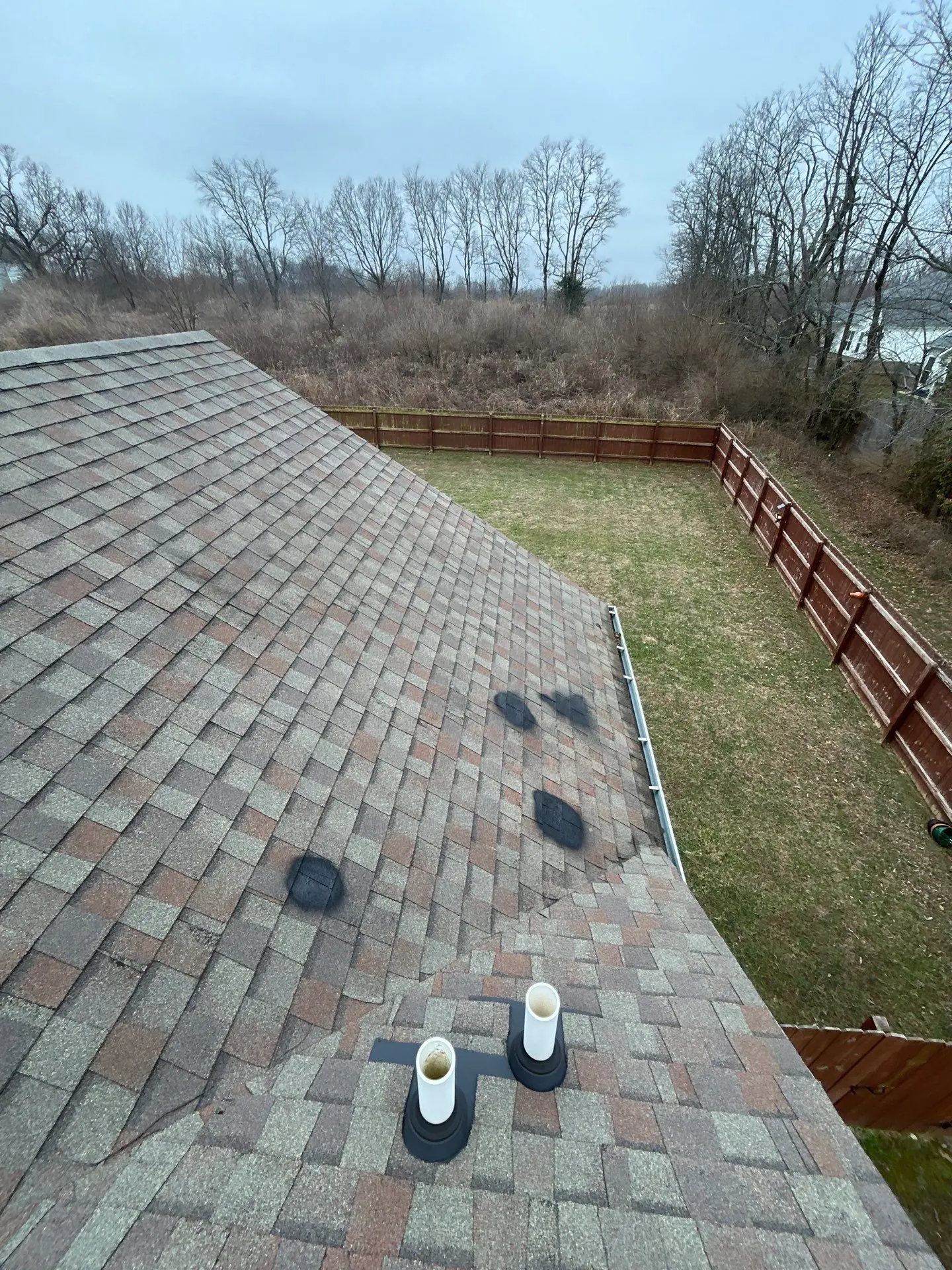 Residential asphalt shingle roof with visible discoloration and granule loss near vent pipes indicating roof aging and wear.