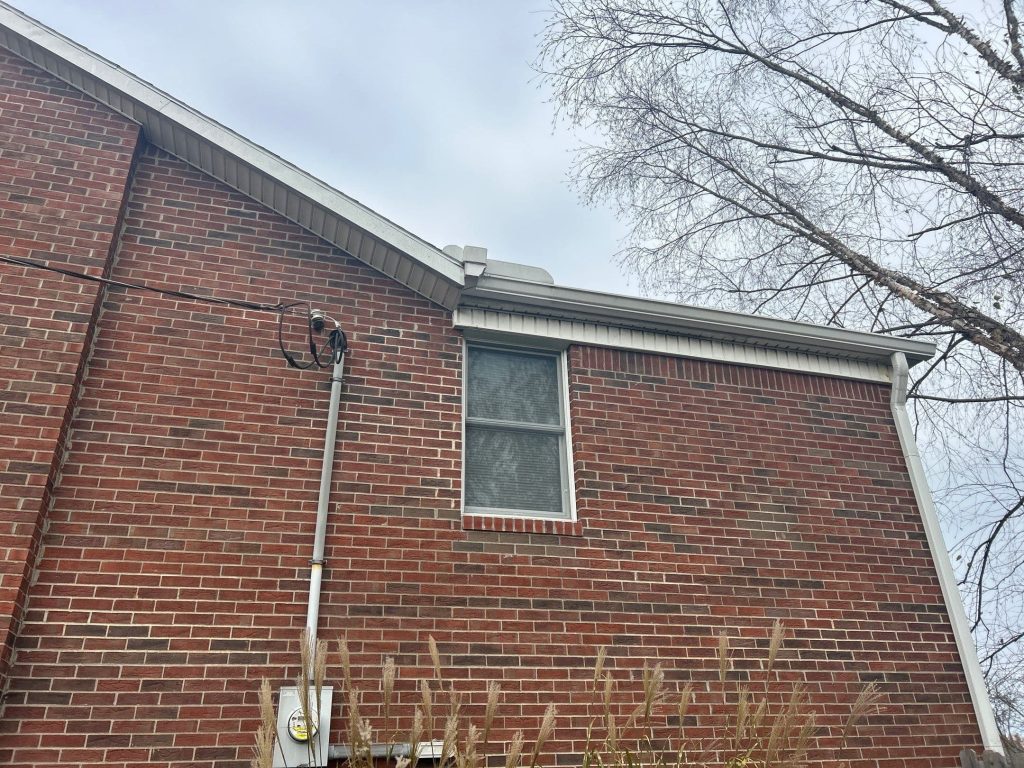 Residential brick home with installed gutter and downspout system for rainwater drainage.