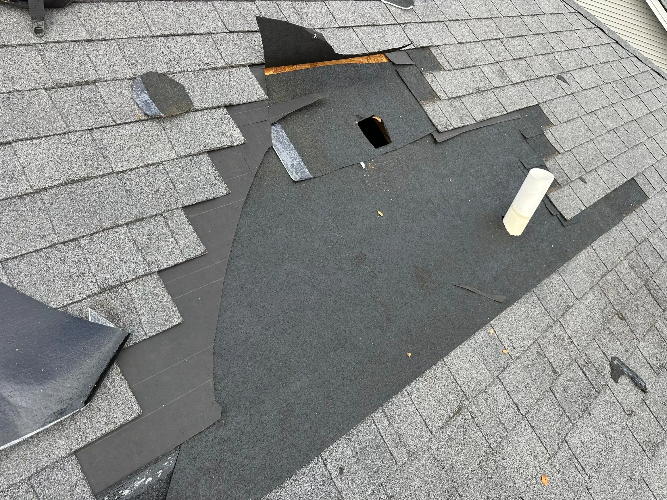 Residential asphalt shingle roof with missing and torn shingles exposing roof underlayment and decking near vent pipe.