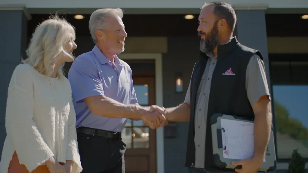 AIC Roofing and Construction team member shaking hands with a satisfied homeowner in front of their home. Contractor shaking hands with homeowners during a roof inspection and siding inspection consultation outside their home.