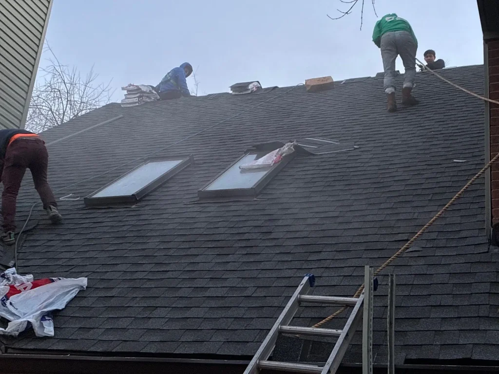 Roofing crew installing asphalt shingles around skylights during roof repair in Lexington Kentucky