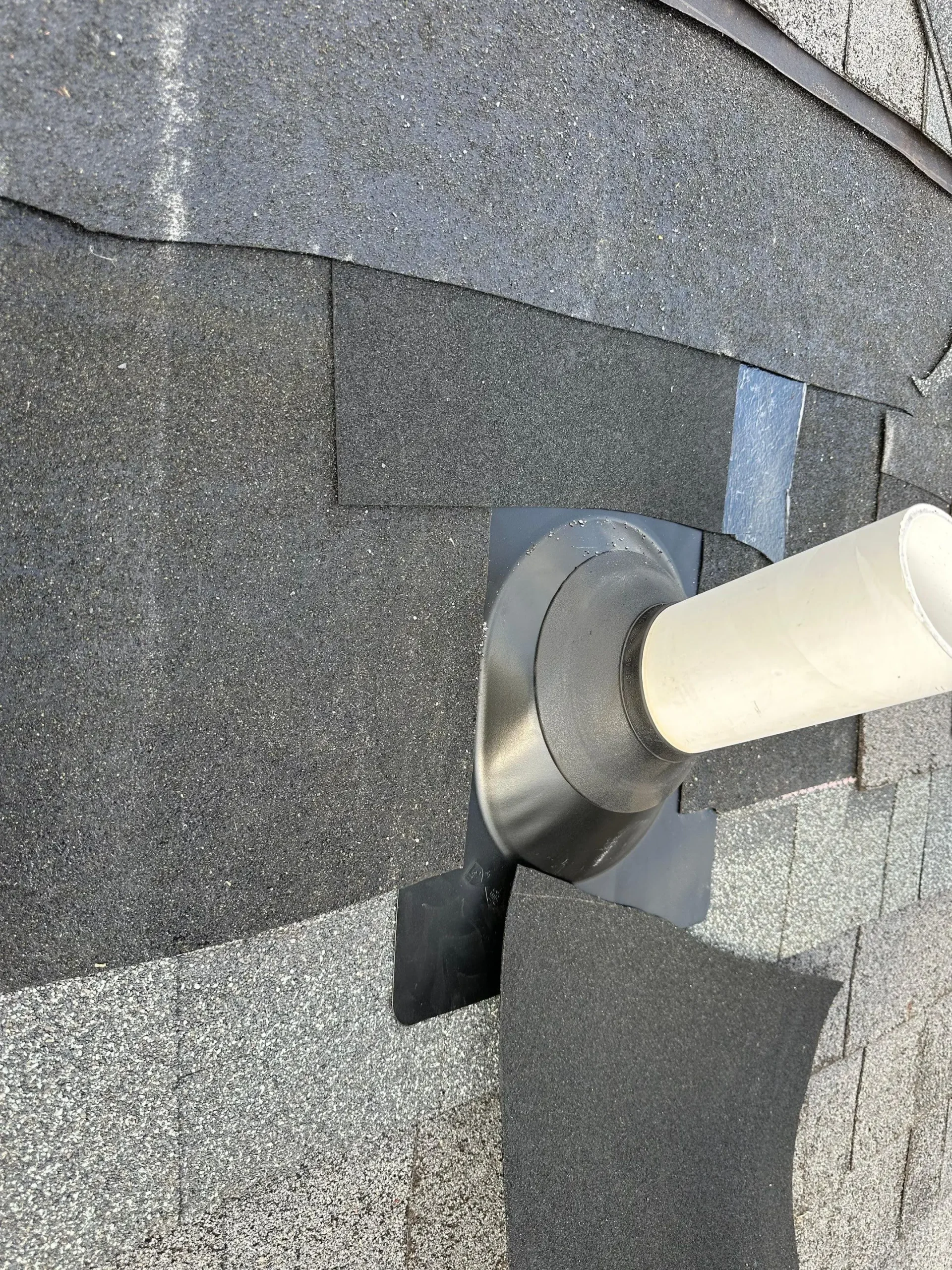 Close-up of residential roof vent pipe with newly installed flashing and surrounding asphalt shingle repair.