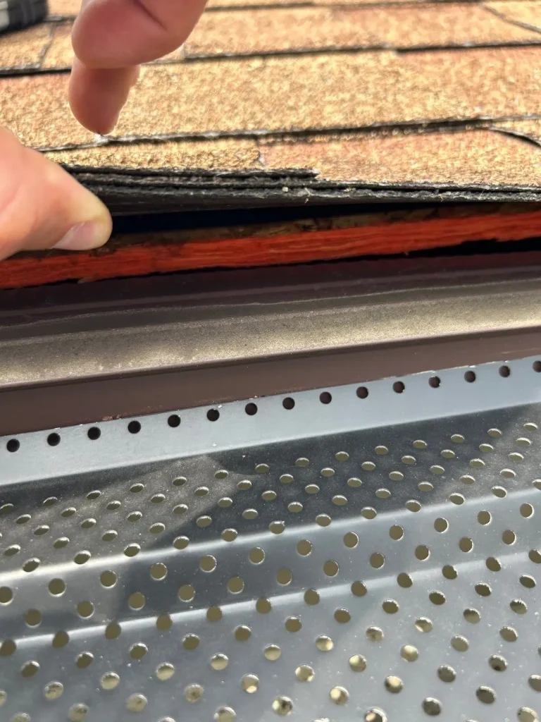 Metal gutter guard installed at roof edge with shingles lifted in Lexington KY