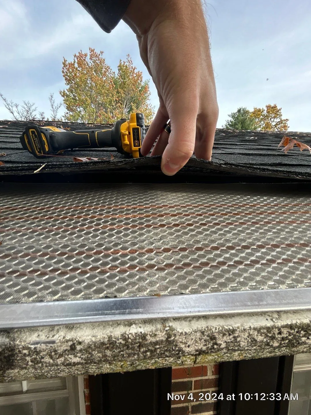 Micro-mesh gutter guard being installed under shingles with a drill in Irvine, KY