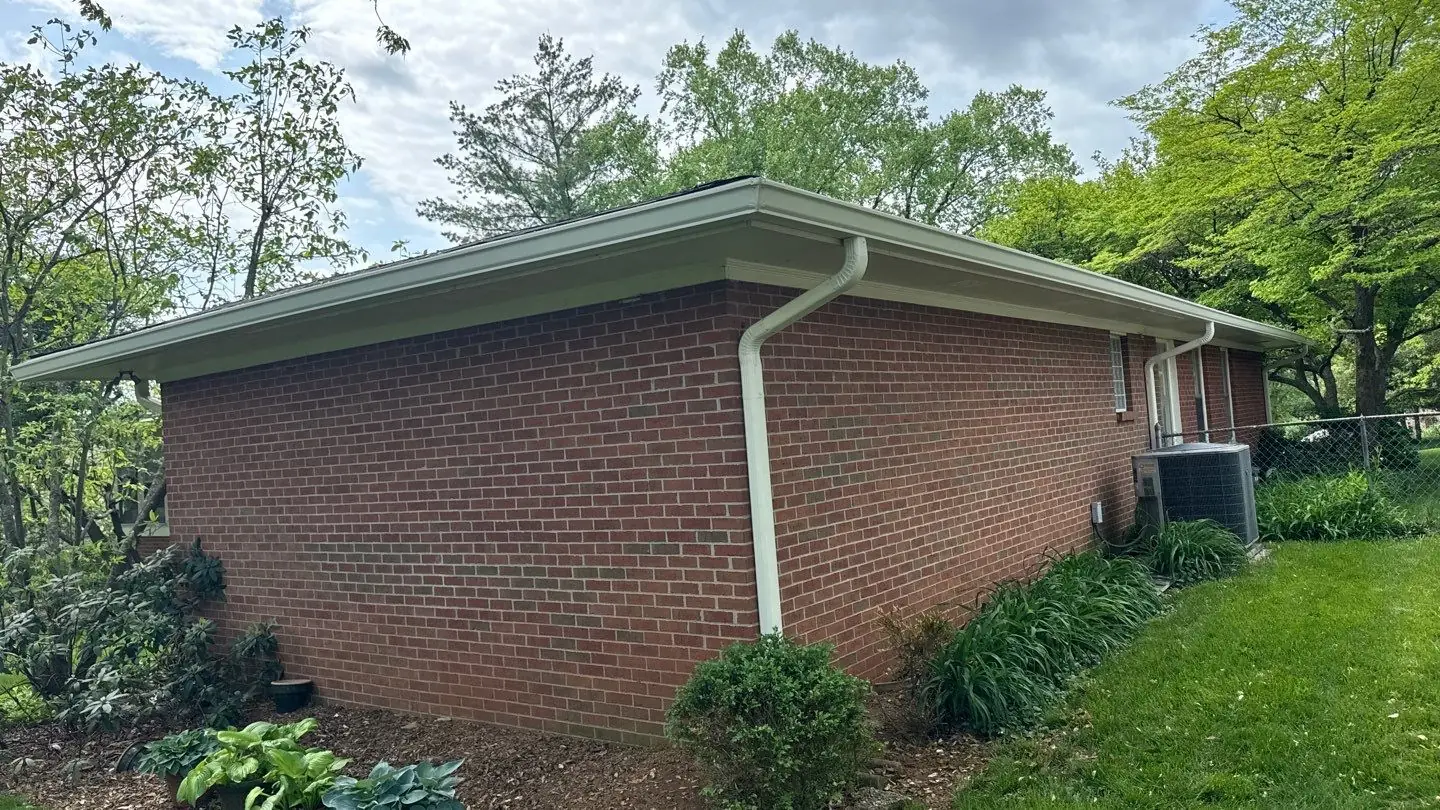 White downspout running down the corner of a brick home, directing rainwater away from the foundation