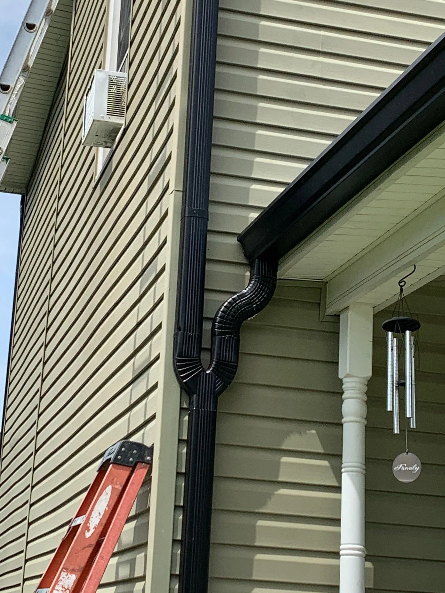 New black gutter and downspout with an offset elbow on a green-sided home in Irvine, KY.