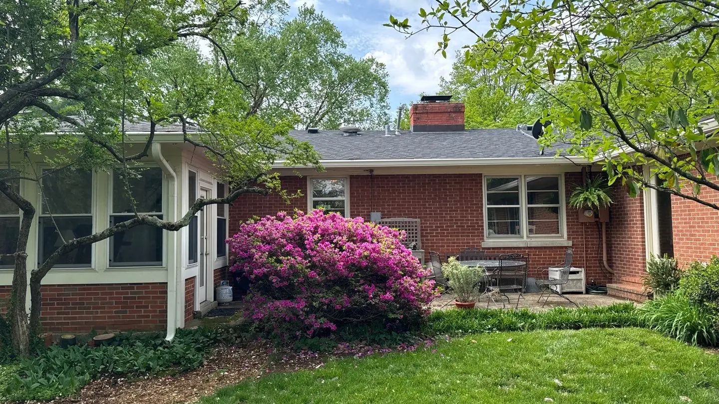White gutters running along the roofline of a brick home with a downspout carrying water away from the foundation