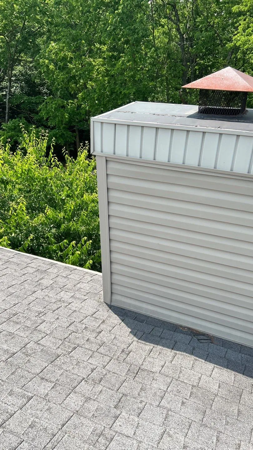 Vinyl-sided chimney chase with a metal cap on a gray shingle roof in Lancaster, KY