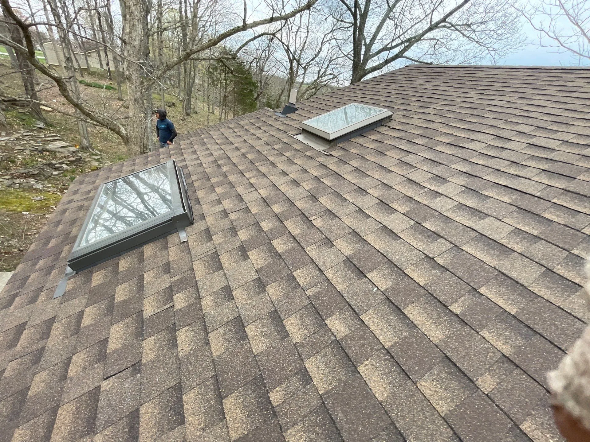 Two skylights on a brown shingle roof with a worker nearby in Lancaster, KY