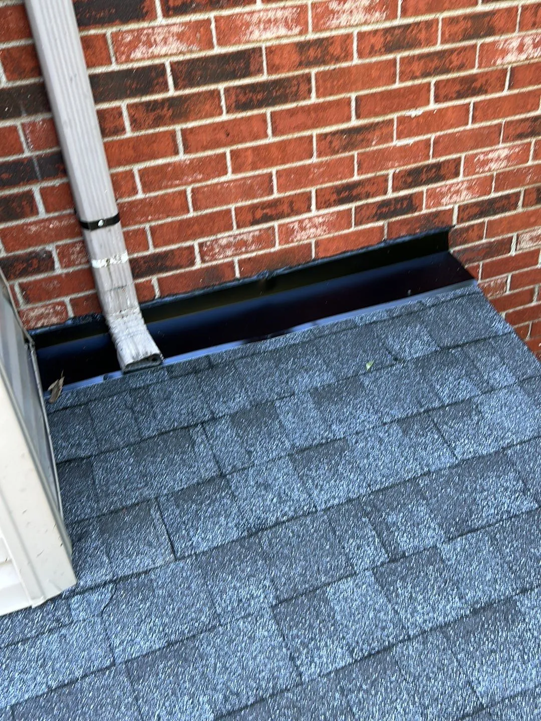 Flashing where a shingle roof meets a brick wall beside a downspout in Mt. Sterling, KY