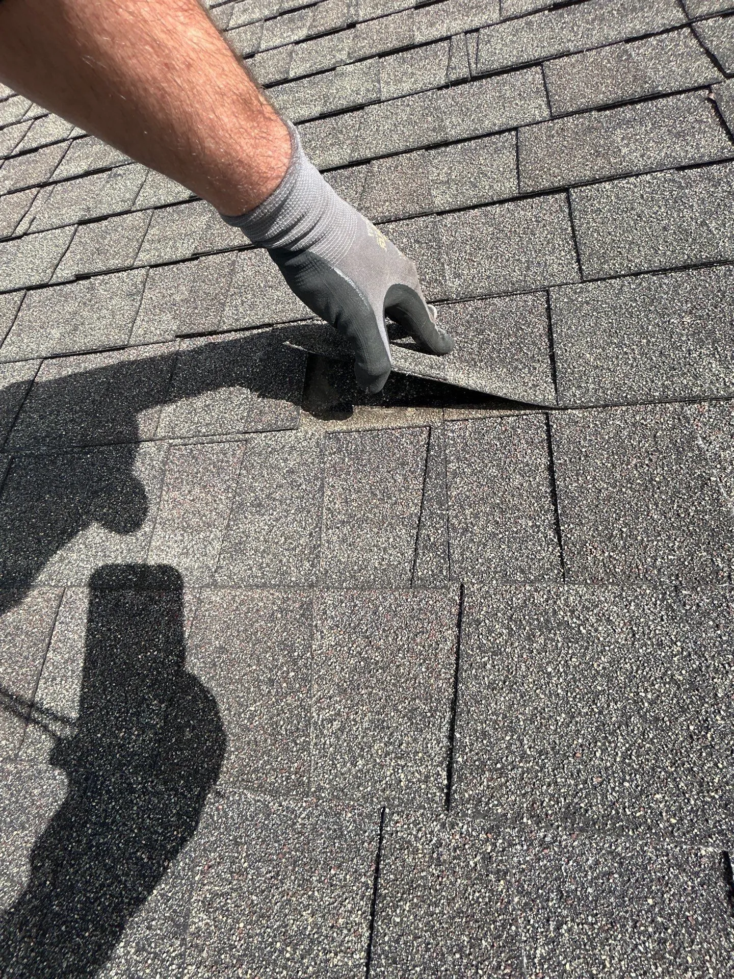 Gloved hand lifting a shingle tab during a roof inspection in Mt. Sterling, KY