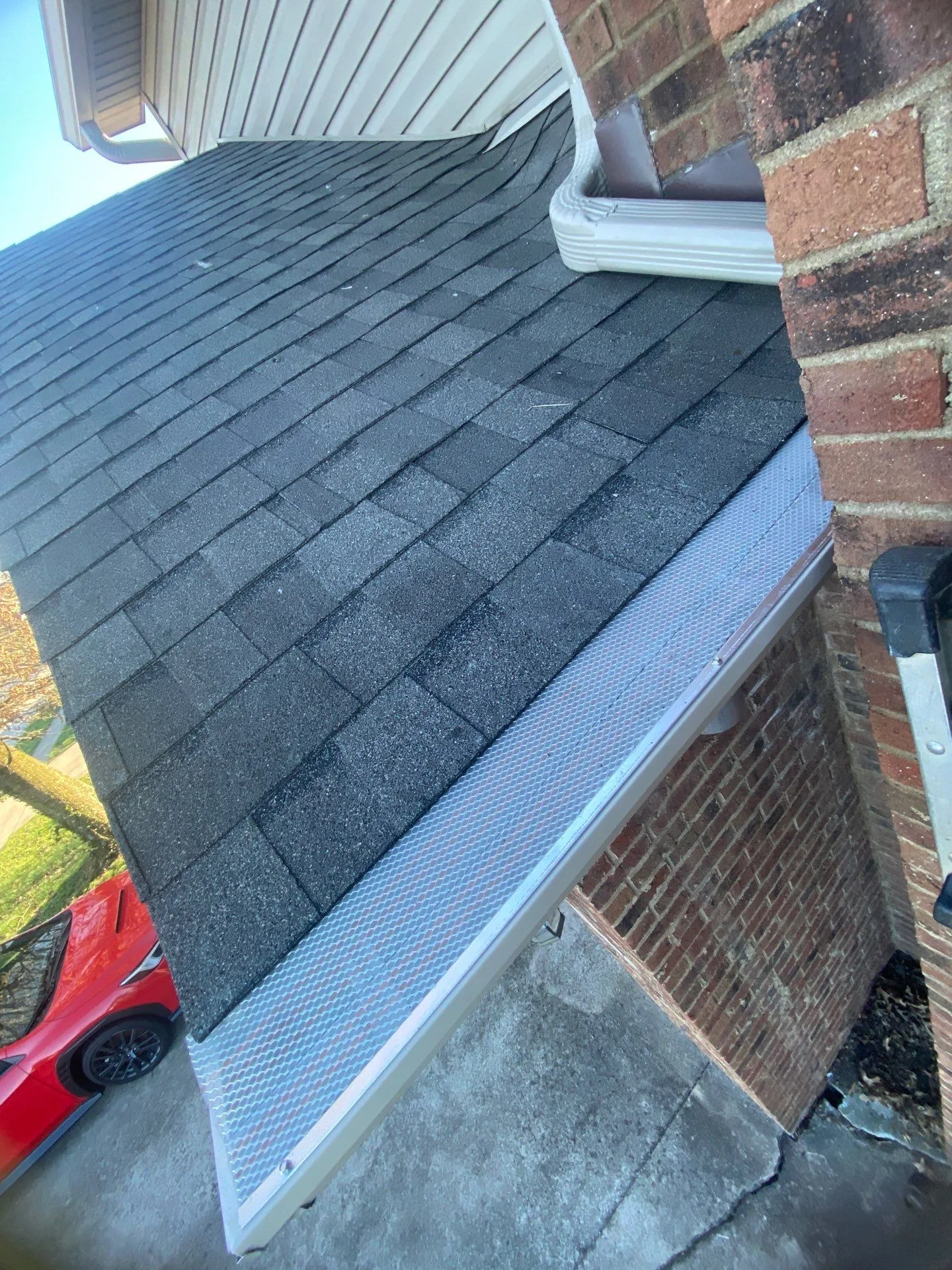 Mesh gutter guard on a shingle roof beside a brick wall on a Lancaster, KY home.