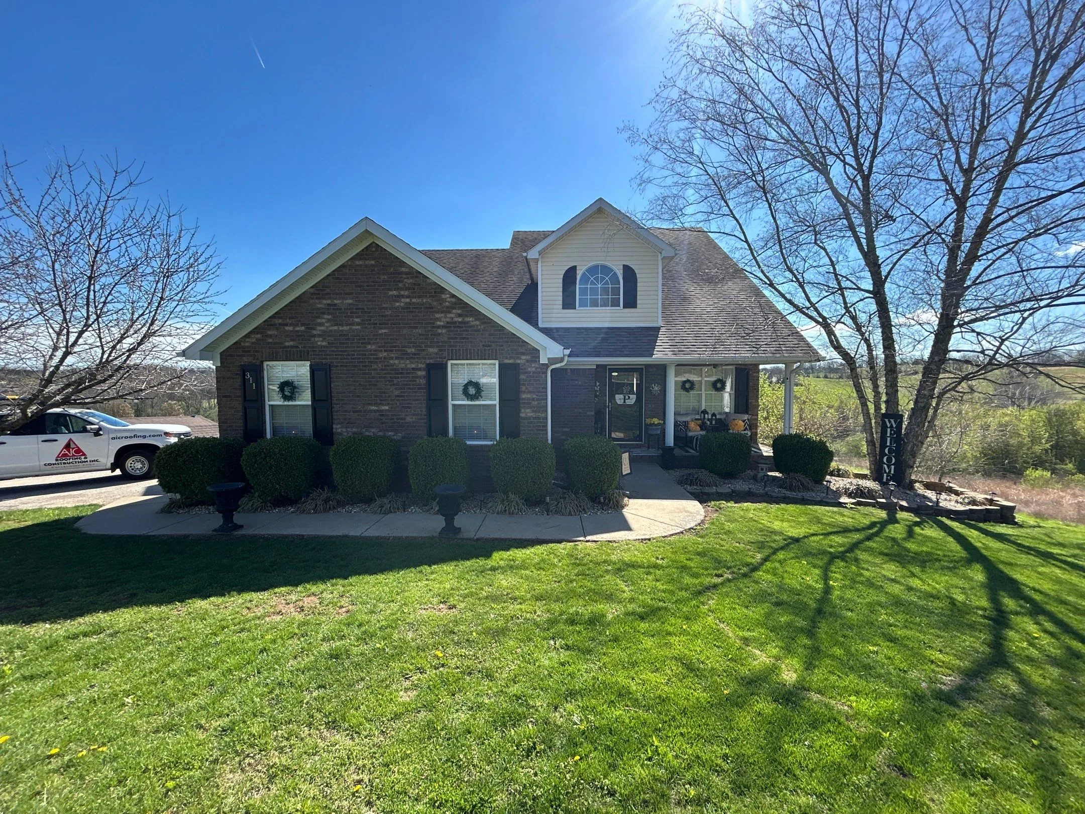 Brick two-story home with new gutters and an AIC Roofing truck in the driveway in Lancaster, KY.