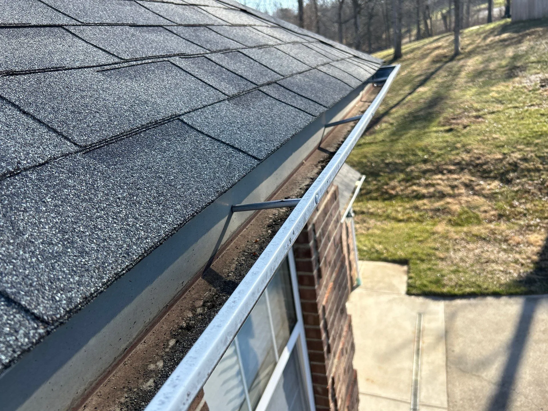 Weathered gutter with dirt and debris along a shingle roof edge on a Waco, KY home.